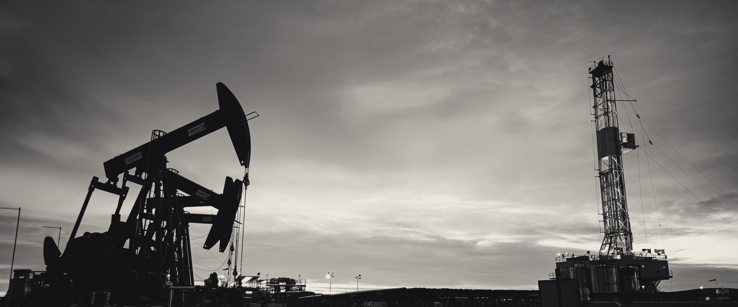 Pump jack and drilling rig at dusk